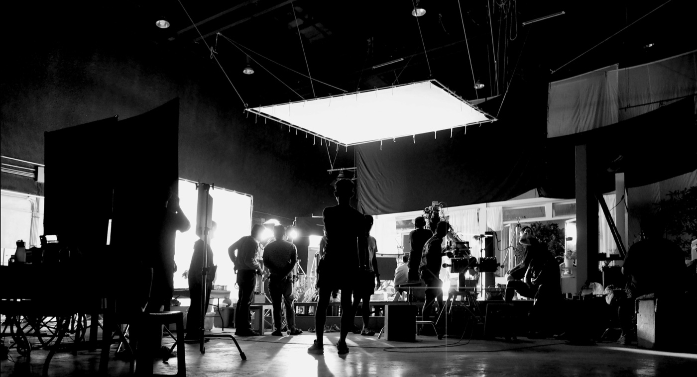 Film crew working beneath a large overhead light on a soundstage